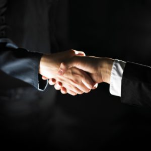 two people's hands shaking with suits on their arms