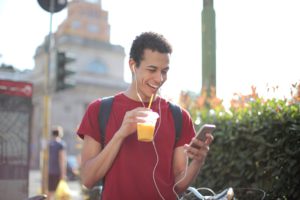 man with an orange drink in one hand laughing while looking at his cell phone in another hand.