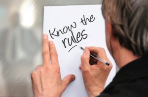 caucasian man writing "know the rules" on a piece of paper pinned against the wall.