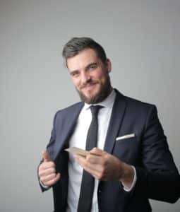 caucasian man in a suit with a card in one hand and the other holding his suit jacket