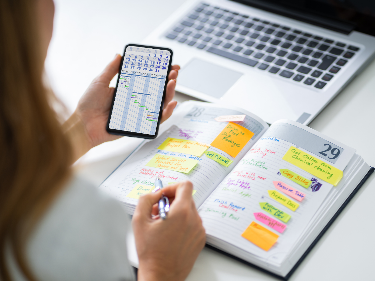 Person organizing tasks with a planner filled with colorful sticky notes and a digital calendar on their phone.